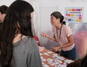Une animatrice explique un jeu de cartes à une visiteuse, devant l’affiche du Pique-nique linguistique.