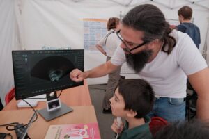 Un animateur montre à un enfant l’image échographique de sa propre langue sur un écran, l’enfant tenant la sonde sous son menton.
