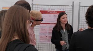 Une animatrice explique une affiche sur la pragmatique, l’étude du sens en contexte, à un groupe de visiteurs.
