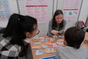 Une animatrice soumet des slogans de publicités alimentaires à deux jeunes visiteurs, pour l’atelier « Persuasion entre les lignes ».
