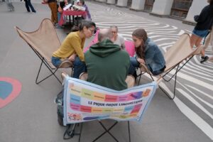 Des visiteurs jouent au Pique-nique linguistique en plein air, installés dans des fauteuils autour du plateau de jeu coloré.